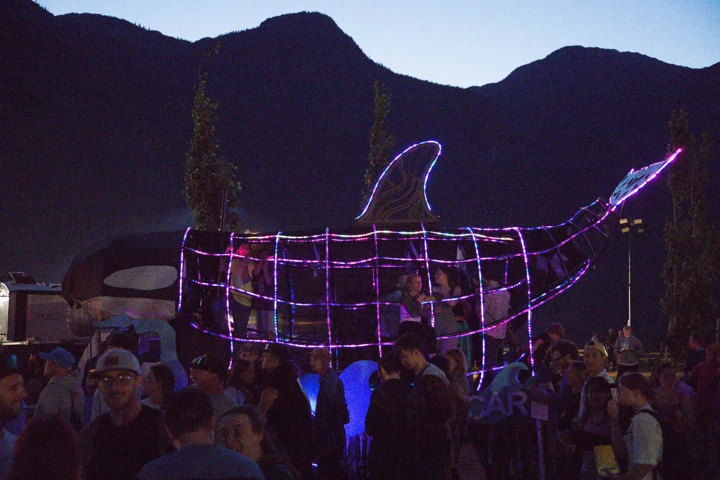 The Orcar at dusk traced in pink and blue LED rope with a crowd gathered around it