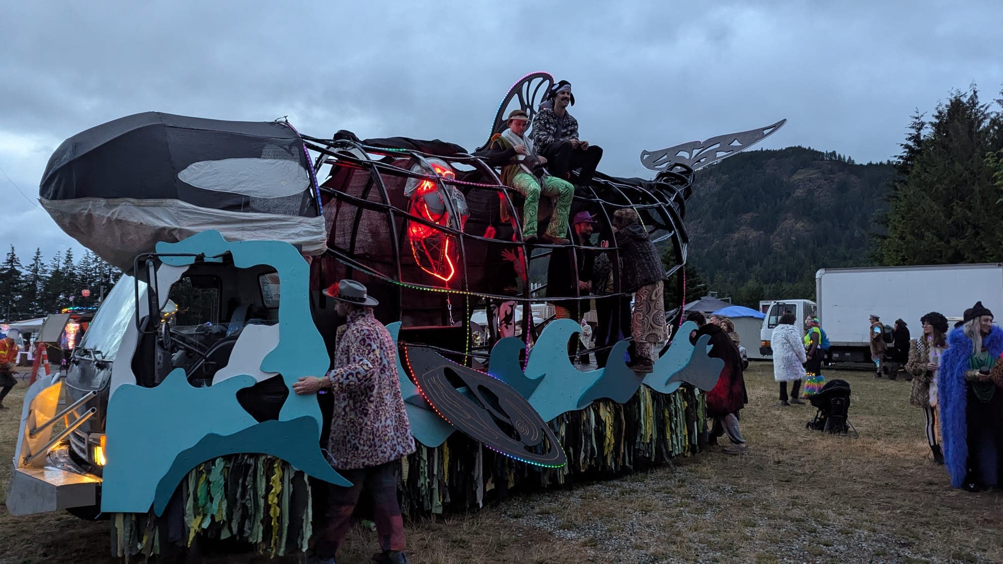 The Orcar at dusk with LED ropes lit, riders inside the body and climbing the frame