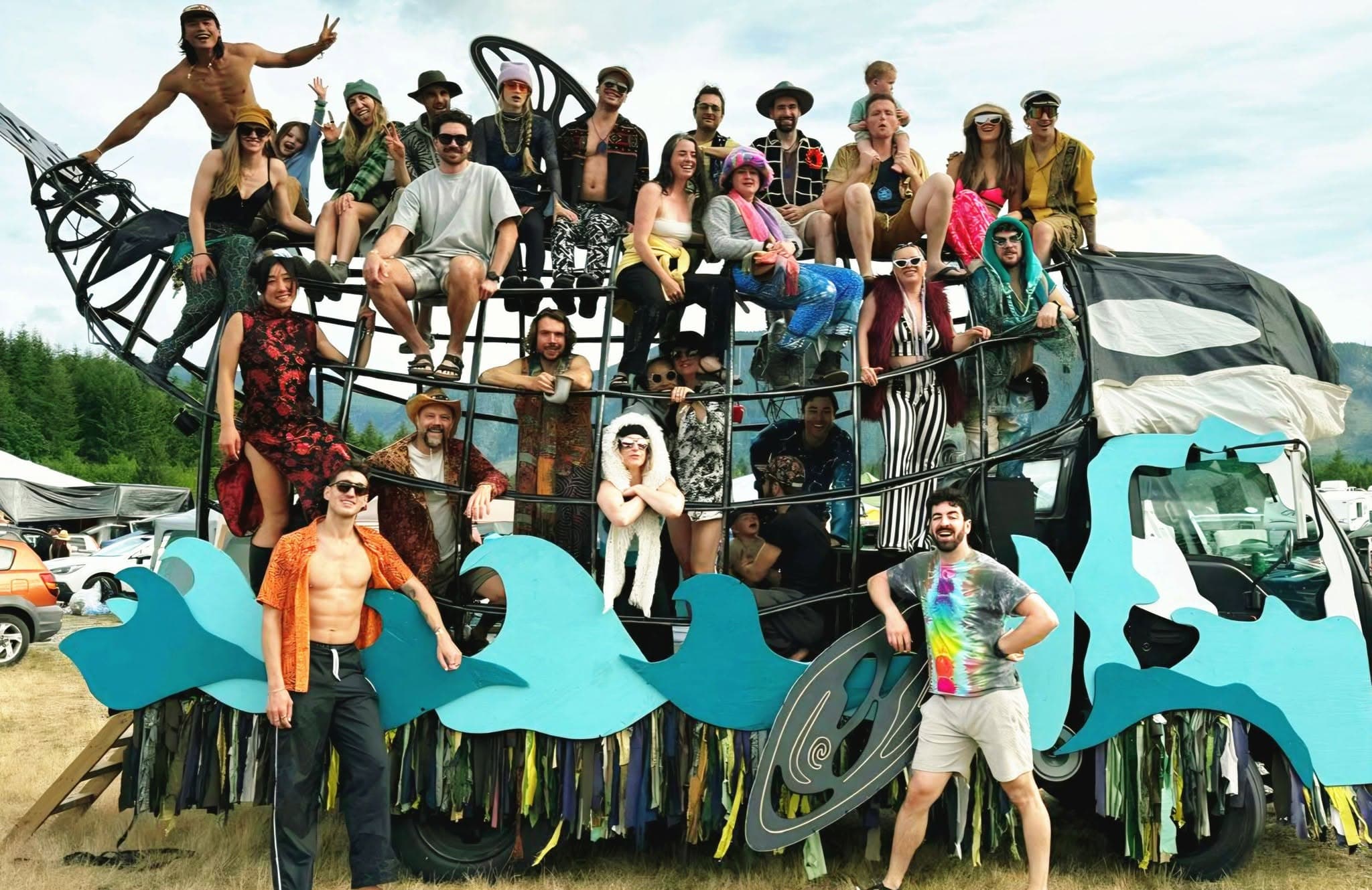 Thirty people posing on and inside the Orcar's steel frame in a festival field